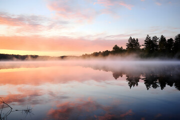 Fototapeta premium Tranquil Morning at a Lake Cabin: Vivid Sunrise Reflecting off Calm Waters with Silhouetted Pier