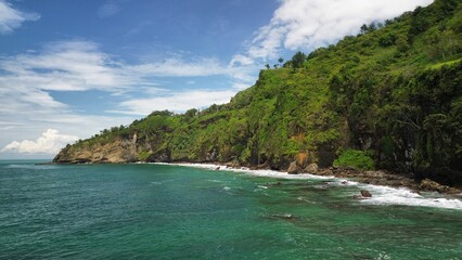 Aerial drone view of coastline with hills and trees, as well as view of coral cliffs and sea with waves from the ocean in Menganti Beach Kebumen Central Java Indonesia