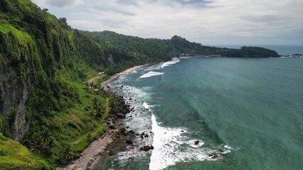 Aerial drone view of coastline with hills and trees, as well as view of coral cliffs and sea with waves from the ocean in Menganti Beach Kebumen Central Java Indonesia