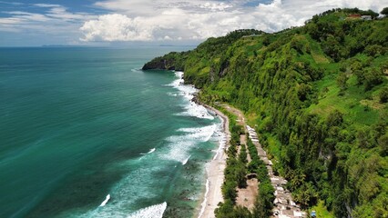 Aerial drone view of coastline with hills and trees, as well as view of coral cliffs and sea with waves from the ocean in Menganti Beach Kebumen Central Java Indonesia