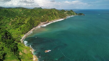 Aerial drone view of coastline with hills and trees, as well as view of coral cliffs and sea with waves from the ocean in Menganti Beach Kebumen Central Java Indonesia