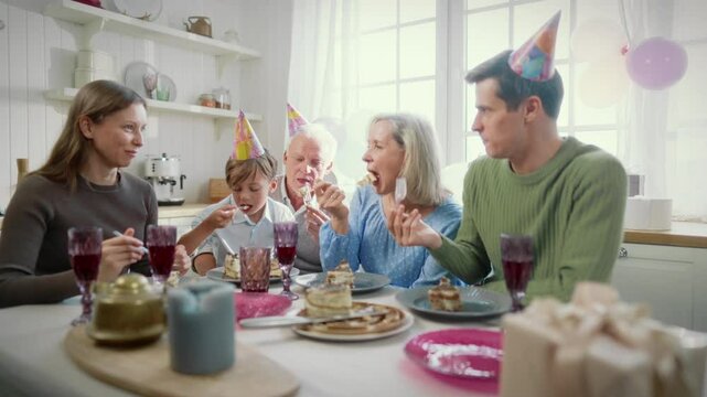 Cheerful people of three different generations celebrating birthday of child boy . Parents and grandparents congratulating cute funny little kid, carefree men and women eating tasty cake in kitchen