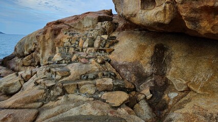 A rocky coastal landscape with scattered boulders in Hon Chong cape rocks garden on the Nha Trang beach, Vietnam with a calm sea and mountains in background.