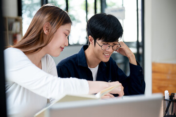 Two young Asian college students are studying and preparing for an exam together in a coffee shop.