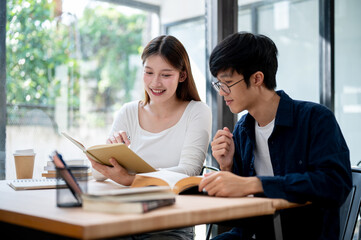Two young Asian college students are studying and preparing for an exam together in a coffee shop.