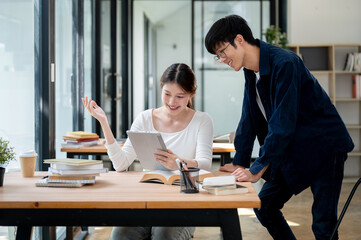 Two positive Asian college students are looking at a tablet screen and discussing.