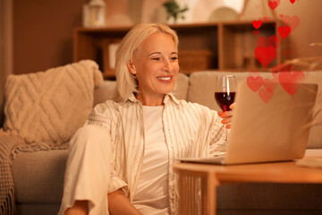Mature woman with wine and laptop on table having online date at home in evening