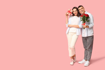 Loving young couple with gift box and bouquet of beautiful roses on pink background. Celebration of Saint Valentine's Day