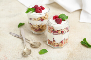 Glass and jar of tasty granola with yogurt on light background