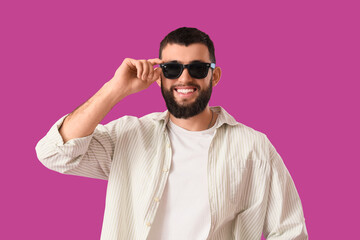 Obraz premium Handsome young happy man in stylish sunglasses on purple background