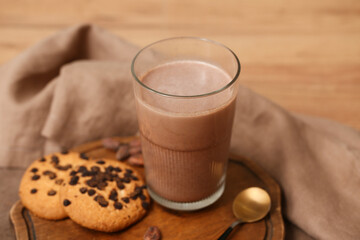 Glass of sweet chocolate milk and tasty cookies on wooden background