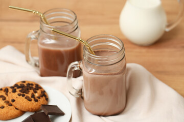 Mason jars of sweet chocolate milk and plate with tasty cookies on wooden background