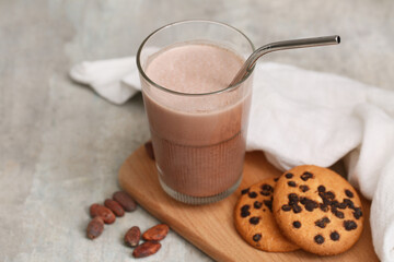 Glass of sweet chocolate milk with cocoa beans and tasty cookies on grey background
