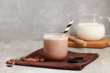 Glass of sweet chocolate milk and cocoa beans on grey background