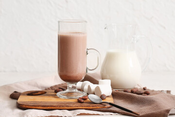 Glass cup of sweet chocolate milk with marshmallows and cocoa beans on white background