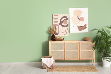 Chest of drawers, pictures and houseplant near green wall in room