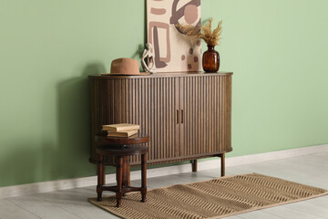 Chest of drawers with pampas grass, picture and books on stool near green wall in room