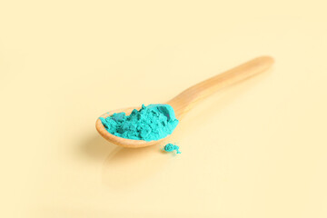 Wooden spoon with bright powder pigment on color background