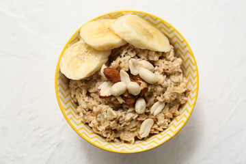 Bowl with tasty oatmeal, banana and nuts on white background, closeup