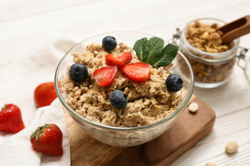 Bowl with tasty oatmeal, berries and mint leaves on white wooden background