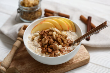 Composition with bowl of tasty oatmeal, pieces of apple and nuts on white wooden background, closeup
