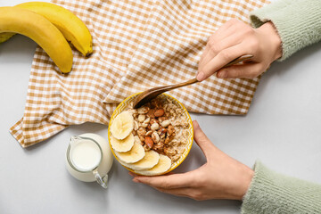 Female hands with tasty oatmeal, nuts and banana in bowl on white background