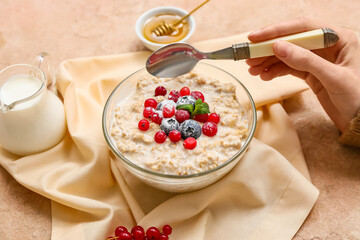 Female hand with tasty oatmeal and berries in bowl on beige grunge background