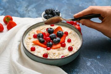 Female hand with tasty oatmeal and berries in bowl on blue grunge background