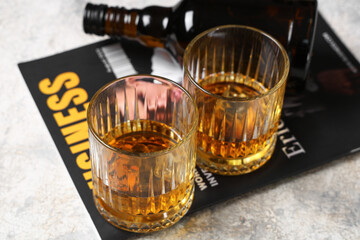 Bottle, glasses of rum and magazine on grey background. Closeup