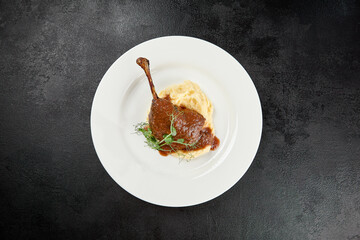 Classic dish french cuisine - roasted duck leg in sauce with garnish on black background. Cooked...