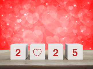 Love icon with 2025 letter on white block cubes on wooden table over blur red love heart background, Happy new year 2025 and Valentines day concept
