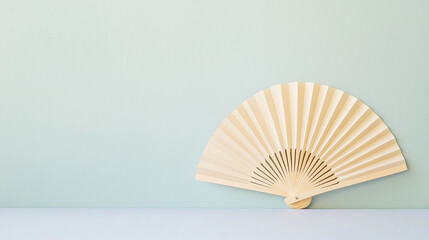 Serene Bamboo Hand Fan: A minimalist image of an elegant, light-colored bamboo hand fan resting on a pale surface against a soft green backdrop.