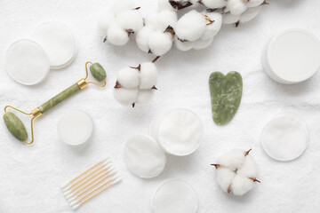 Composition with cosmetic pads, facial massage tools, cream and cotton flowers on light fabric