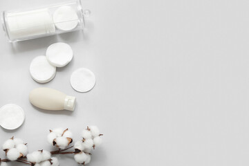 Bottle of cosmetic product, pads and cotton branch on grey background