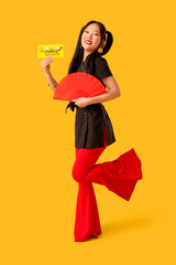 Beautiful Asian woman with paper fan and greeting card for Chinese New Year on yellow background