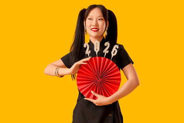 Beautiful Asian woman with paper fan and candles in shape of figure 2026 on yellow background