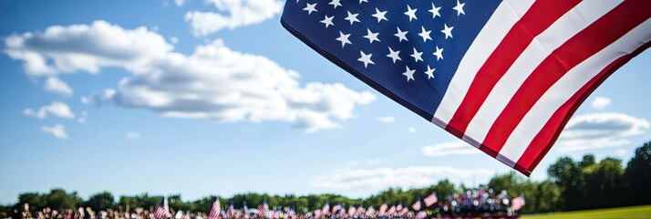 A waving American flag in front of a crowd under a blue sky with clouds.