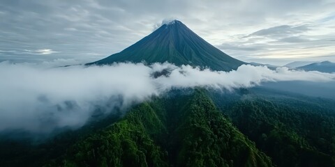 Fototapeta premium A majestic volcano surrounded by lush rainforest, with clouds swirling around its peak