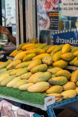 Juicy yellow mangoes are artfully arranged at a lively market stall, capturing the sunlight and...