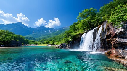 Fototapeta premium Serene waterfall cascading into a crystal-clear mountain lake, surrounded by lush greenery and majestic mountains under a vibrant blue sky.