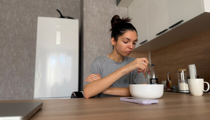 In a contemporary kitchen, a woman sits at the table, savoring her oatmeal for breakfast