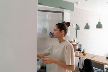 A woman stands in her kitchen opening the fridge to find something to eat during mealtime, surrounded by food items