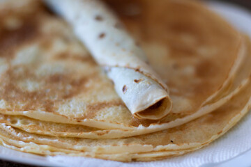 A rolled up crepe with chocolate spread inside of it on a stack of other crepes for breakfast.