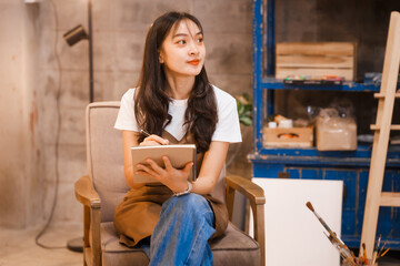 A cute Asian woman, a creative painter, works in her art studio.focuses on her painting,expressing her emotions and ideas through vibrant colors,creating beautiful artwork in a peaceful environment