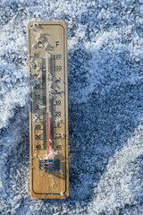 Wooden thermometer lying on a frozen surface covered with ice crystals, indicating freezing...