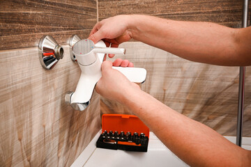 Professional plumber working carefully, installing or repairing bathtub faucet in modern bathroom