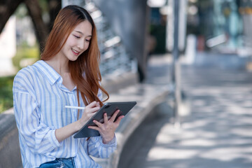 Woman is sitting on a bench and using a tablet