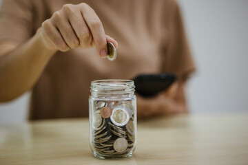 Close up of Asian businesswoman putting coins into piggy bank on table. Saving money, investment, currency concept.