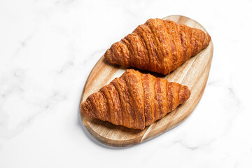 Croissants on wooden cutting board on white marble background