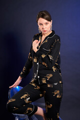 A woman in a black and gold pajama set poses for the camera in a studio against a dark background. The outfit features animal prints, giving it a playful and whimsical look. Confident pose of a woman
